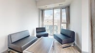 Located at 130 Columbia St W in Waterloo, Ontario, this one-bedroom unit offers a well-organized and efficiently designed layout across a single floor. Light-toned hardwood-style flooring runs throughout the space, creating a cohesive and clean aesthetic from room to room.

The living room is bright and inviting, anchored by large floor-to-ceiling windows that fill the area with natural light and provide open views of the surrounding urban streetscape. The kitchen is thoughtfully equipped with beige shaker-style cabinetry, dark granite countertops, a glass tile backsplash, and black appliances including a refrigerator, electric range, and dishwasher. A pendant light fixture adds a polished touch above the kitchen peninsula, which also serves as a transitional element between the kitchen and living area.

The bedroom is a comfortable and functional space featuring a built-in closet with a hanging rod for storage, a dedicated study desk area, and a large window that introduces natural light and urban views. The clean white walls and neutral finishes throughout contribute to a calm, modern ambiance well-suited for everyday living.

Overall, the unit presents a contemporary and practical design, ideal for those seeking a functional living space in the heart of Waterloo.