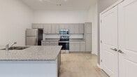 Located at 4815 Market Green Place West in Lakeland, TN, this single-floor, one-bedroom, one-bathroom unit offers a thoughtfully designed layout that maximizes its compact footprint. The kitchen serves as the centerpiece of the home, boasting grey shaker-style cabinetry extending to the ceiling for ample storage, speckled granite countertops, and a full suite of stainless steel appliances including a refrigerator, electric range, microwave, and dishwasher. A peninsula with a double basin sink and pendant lighting overhead adds both functionality and visual interest to the space. Polished concrete floors flow seamlessly throughout the entire unit, lending a modern, low-maintenance aesthetic. The living area is bright and open, with high ceilings that enhance the sense of space. The bedroom is a comfortable size, featuring a window with blinds that allows natural light and outdoor views, along with a ceiling fan. A dedicated closet provides convenient storage. The bathroom is cleanly finished with matching grey cabinetry, granite vanity top, a full tub-shower combination with built-in shelving, and brushed nickel fixtures. The clean, neutral palette and consistent finishes throughout create a cohesive and move-in ready environment.