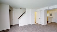 The property at 9217 Kingstree Rd spans two floors, offering a straightforward and functional layout. The interior is finished with neutral white walls throughout, creating a bright and clean aesthetic that provides a versatile backdrop for any furnishing style. Plush carpeted flooring extends across the lower level, adding warmth and comfort underfoot.

A central staircase with a dark wood handrail connects the two floors, serving as a defining architectural element of the main living area. The staircase is framed by a clean white enclosure that integrates seamlessly with the surrounding walls. Adjacent to the staircase, a doorway leads to an additional room or utility space, suggesting practical secondary spaces on the lower level.

Multiple doorways are visible, indicating a well-divided floor plan with distinct areas accessible from the main living space. The low, flat ceiling and recessed layout of portions of the lower level hint at a partially below-grade or basement-level floor, while the upper level provides additional living space above. Overall, the space presents a tidy, move-in ready environment with a simple and functional design.