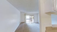 This single-floor space offers a clean, minimalist layout filled with natural light. The main living area is spacious and open, featuring neutral wall-to-wall carpeting that adds warmth and comfort underfoot. Crisp white walls and a textured ceiling contribute to a bright, airy atmosphere throughout.

A standout feature of the living area is the sliding glass door that opens to a private balcony, allowing natural light to flood the interior while framing views of surrounding greenery. The balcony, enclosed by a railing, provides a pleasant outdoor extension of the living space.

The open layout of the main area creates a versatile environment suitable for a variety of furniture arrangements and uses. The transitions between spaces are defined by subtle architectural details, including a prominent structural column that adds character to the interior design.

Overall, the space presents a simple yet functional design with a neutral color palette, making it easy to personalize and style. The combination of generous natural light, soft carpeting, and outdoor access gives this space a welcoming and comfortable ambiance ideal for everyday living.