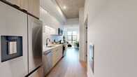 Located in Denver's vibrant West Side neighborhood, this thoughtfully designed one-bedroom, one-bathroom residence offers a contemporary urban living experience. The space showcases an industrial-modern aesthetic, highlighted by exposed concrete ceilings that contrast beautifully with crisp white walls and light wood-tone flooring throughout.

The galley-style kitchen is well-appointed with stainless steel appliances — including a French door refrigerator, dishwasher, and gas range — complemented by white upper cabinetry, natural wood lower cabinets, a white subway tile backsplash, and an undermount sink with a matte black faucet. The kitchen flows seamlessly into the living area, which is anchored by oversized, black-framed floor-to-ceiling windows offering sweeping views of the Denver skyline and filling the space with abundant natural light.

The bedroom features plush carpeting, exposed concrete ceiling detail, a large window with city views, and access to two closets. The full bathroom is finished with a light wood vanity, white countertop, a large mirror, matte black fixtures, and a tiled tub-shower combination. A dedicated laundry area and hallway with in-wall utility access complete this efficiently laid-out residence.
