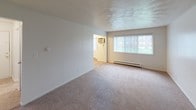 Located at 1219 E Bellows St in Mount Pleasant, Michigan, this single-story unit offers a straightforward, functional layout designed for comfortable everyday living. The floor plan reveals a well-organized arrangement of interconnected rooms, with neutral-toned walls and light carpet throughout the living and sleeping areas creating a clean, cohesive aesthetic.

The spacious living area is bright and open, featuring large windows with vertical blinds that allow natural light to filter in, along with baseboard heating and an included wall-mounted air conditioning unit for year-round climate control. The room opens conveniently toward the kitchen corridor, supporting easy flow between living and dining spaces.

The galley-style kitchen is efficiently designed, featuring warm oak cabinetry on both upper and lower levels, laminate countertops, a double-basin sink, and white appliances including a coil-top range, refrigerator, and dishwasher. Tile flooring adds durability in this functional workspace, and a doorway at the end leads to additional areas of the unit.

Two carpeted bedrooms each offer natural light through window treatments and baseboard heating. The full bathroom is outfitted with tile flooring, a tiled tub-shower combination, a vanity with an integrated sink, and a well-lit mirror. Overall, the space maintains a practical, well-maintained character throughout.