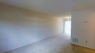 This two-floor residential space offers a clean, functional layout designed with simplicity and practicality in mind. The interior is characterized by neutral, light-colored walls that create a bright and airy atmosphere throughout. The main living area features wall-to-wall carpeting in a soft, neutral tone, providing a comfortable underfoot feel and a cohesive look across the space. A sliding glass door fitted with vertical blinds serves as a notable architectural feature, allowing natural light to filter into the room while offering privacy and light control. The door also provides direct access to an exterior area, enhancing the overall sense of openness. The ceilings are smooth and finished in white, contributing to the clean aesthetic of the interior. Subtle details such as flush-mounted ceiling lighting and standard electrical outlets are thoughtfully placed throughout. The layout spans two floors, offering separation between living and private spaces, which adds versatility and functional zoning to the overall floor plan. The neutral palette and open feel of the rooms make the space highly adaptable to a variety of interior styles and furnishing choices.
