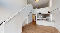 This two-story residence is defined by its dramatic double-height living area, where floor-to-ceiling windows flood the main level with abundant natural light and create an open, airy atmosphere. A sleek staircase with white railings anchors the space, connecting the two floors while enhancing the sense of vertical volume.

The kitchen is thoughtfully designed with dark cabinetry, granite countertops, a peninsula with an undermount sink, and a full suite of stainless steel appliances, including a range, microwave, and refrigerator. Industrial-style pendant lights hang above the peninsula, adding a contemporary touch. The main level also features a half bathroom with a pedestal sink and wood-look flooring.

Upstairs, the bedrooms offer a quieter retreat; one features soft carpeting with a bold accent wall, while another showcases warm hardwood-style flooring and a walk-in closet. The upper level is served by two full bathrooms, each finished with granite-topped dark vanities, wood-look flooring, and glass-enclosed showers. Throughout, the clean white walls and modern finishes create a cohesive, contemporary aesthetic.