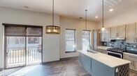 Located at 1212 S Rangeline Rd in Carmel, Indiana, this single-floor residence offers a thoughtfully designed open-concept layout finished with contemporary details throughout. Wide-plank wood-look flooring runs continuously across the living and kitchen areas, anchoring the space with a warm, cohesive aesthetic.

The kitchen serves as the centerpiece of the unit, featuring a large center island with an integrated sink, white quartz countertops, and a built-in wine rack beneath. Light wood shaker cabinetry lines the walls, complemented by a striking teal geometric tile backsplash and a full suite of stainless steel appliances including a gas range, microwave, and French door refrigerator. Pendant lighting above the island adds both function and style, while elevated ceilings enhance the sense of openness.

The living area is bright and airy, benefiting from large windows fitted with roller shades and a glass-panel door that opens to a private balcony. A ceiling fan adds comfort to the space.

The bathroom presents a clean, modern aesthetic with white subway tile surrounding the soaking tub and shower, matte black fixtures, a floating vanity with an integrated basin, and wall-mounted sconce lighting flanking a framed mirror. The overall design balances modern finishes with functional living in a well-located Carmel address.