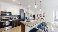 This single-floor residence showcases a contemporary open-concept design with light wood-look flooring flowing throughout. The kitchen serves as a central hub, featuring dark espresso cabinetry contrasted by white upper cabinets, a textured tile backsplash, stainless steel appliances, and a granite-topped island with pendant lighting overhead and bar seating. The kitchen connects seamlessly to a dedicated dining area with clean white walls and an adjoining living room that benefits from abundant natural light through large sliding glass doors opening to a private patio.

The layout includes two bedrooms, each with natural light from windows fitted with blinds. The primary bedroom features a ceiling fan and slider access, while the secondary bedroom offers a more intimate, cozy atmosphere. Two bathrooms serve the unit: one with a walk-in glass-enclosed shower with a built-in bench and granite countertops, and a second featuring a full soaking tub with a tiled surround. Both bathrooms include white cabinetry for ample storage. The overall design balances modern finishes with a warm, inviting ambiance throughout.