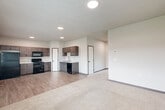 Located at 5722 Sunnybrook Dr in Sioux City, Iowa, this two-story home offers a practical and well-organized layout spread across two levels. The ground floor hosts the main living areas, including an open-concept kitchen and living room finished with wood-look plank flooring. The kitchen is equipped with dark cabinetry, black appliances including a range, microwave, dishwasher, and refrigerator, along with a sink and ample counter space. Recessed lighting illuminates the combined living area, which transitions seamlessly between the kitchen and carpeted living space. Also on the ground floor is an attached garage with an automatic opener, concrete flooring, and a direct interior access door. A carpeted staircase with a metal handrail connects the floors via a hallway. The upper level features two bedrooms, including a spacious primary bedroom, both carpeted and filled with natural light from windows overlooking the outdoors. A closet with double doors is featured in one of the bedrooms. Two bathrooms serve the home, one of which includes wood-look tile flooring, a large window, and modern black hardware accents. Neutral tones and clean finishes throughout give the home a bright, move-in ready feel.