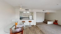 This two-story home offers a practical and comfortable layout designed for everyday living. The main level features an open-concept design that integrates the kitchen, dining area, and living space into a cohesive, flowing environment. The kitchen is equipped with white cabinetry, a built-in range, a refrigerator, and a countertop that doubles as a breakfast bar with bar stool seating — ideal for casual dining or entertaining. Under-cabinet lighting adds a functional touch to the workspace. Adjacent to the kitchen, the dining area accommodates a glass-top dining table, adding a light and airy feel to the space. Wood-look flooring runs throughout the main level, providing a warm and durable surface, while a ceiling fan overhead ensures comfortable airflow. A short staircase leads to the second floor, where carpeted steps hint at a cozier, more private retreat. The textured ceilings and clean white walls give the interior a bright and neutral palette, offering a versatile backdrop for any décor style. Central air conditioning vents are present throughout, ensuring year-round climate comfort. This home combines functional design with approachable living spaces across both of its floors.