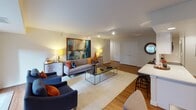 Located at 4001 N 9th Street in Arlington, Virginia, this single-floor residence offers a thoughtfully designed layout with distinct living, dining, and sleeping areas connected by warm hardwood flooring. The expansive living room serves as the centerpiece of the home, featuring track lighting, a large-scale abstract artwork, floor-to-ceiling drapes, and a sliding glass door that invites natural light and outdoor views of the surrounding Arlington cityscape. A tufted sofa, paired armchairs, and a sleek coffee table complete the inviting arrangement.

The galley-style kitchen is outfitted with white shaker cabinetry, white quartz countertops, a subway tile backsplash, and stainless steel appliances, including a range, microwave, and refrigerator. Adjacent to the kitchen, a breakfast bar with bar seating provides a casual dining option, while a separate dining area accommodates a full table and chairs beneath track lighting and wall-mounted display shelving.

The bedroom features plush carpeting, large windows with patterned drapery offering urban views, recessed lighting, and ample closet space. Two bathrooms serve the residence — one with a tub-shower combination and the other with a clean, white vanity and updated fixtures — both finished in a crisp, neutral palette.