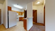 This single-floor residential unit offers a well-organized layout designed for comfortable everyday living. The kitchen is outfitted with warm oak cabinetry, a full suite of white appliances including a refrigerator, electric range, microwave, and dishwasher, all set atop neutral tile flooring. A peninsula breakfast bar separates the kitchen from the adjoining living and dining areas, creating an open and connected flow throughout the space. The living area is generously proportioned, featuring soft wall-to-wall carpeting and a sliding glass door that opens to a private balcony, allowing natural light to fill the room and providing pleasant outdoor views. The bedroom offers carpeted flooring, neutral walls, and closet access, making it a quiet and practical retreat. The full bathroom is cleanly appointed with tile flooring, a tub-shower combination equipped with safety grab bars, a wood-trimmed vanity with a white countertop, and a large mirror. Throughout the unit, consistent trim work, neutral tones, and flush-mount lighting contribute to a cohesive and functional aesthetic. The layout as a whole provides a practical and comfortable living environment suited to a variety of needs.
