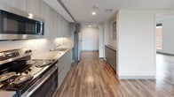This single-floor, two-bedroom, two-bathroom residence showcases a clean, contemporary design with consistent wood-look flooring running throughout every room. The open-concept living and kitchen area forms the heart of the space, where a well-appointed kitchen features light wood-toned cabinetry, subway tile backsplash, stainless steel appliances including a range, microwave, and refrigerator, and a sleek countertop with an undermount sink. The living area flows naturally from the kitchen, offering ample room for furnishings against a neutral gray accent wall.

Both bedrooms are generously sized, featuring large windows that invite abundant natural light and provide views of surrounding greenery and urban scenery. Each bedroom includes a closet with built-in rod storage. The two bathrooms are finished in a crisp, modern style with wood-look flooring, floating white vanities, framed mirrors, and clean white fixtures. One bathroom features a walk-in shower with a mosaic tile floor, while the second includes a soaking tub with shower combination. Recessed lighting and a neutral color palette throughout contribute to a bright, cohesive ambiance.