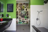 This single-room pet washing and grooming station is thoughtfully designed to provide a clean, functional, and welcoming environment for pet owners and their dogs. The space is finished with durable gray tile flooring and white subway tile wainscoting that extends along the lower walls, creating a hygienic and easy-to-maintain surface throughout. Vibrant green paint above the wainscoting adds a lively, cheerful energy to the room.

A standout feature is the floor-level tiled bathing basin, equipped with a central drain, making it easy to wash pets without the need for heavy lifting. Adjacent to the wash area is a grooming station with a dark granite countertop, an integrated sink with a soap dispenser, paper towel dispensers, and a wall-mounted professional pet dryer — providing everything needed to bathe and dry pets in one place.

A built-in white countertop with seating offers a convenient space for pet owners to set belongings or prepare their pets. The focal point of the room is a full photo collage wall mural featuring a lively arrangement of dog portraits in various breeds and poses, giving the space a warm, pet-friendly character. A glass-paneled entry door allows natural light to filter in while offering views of the surrounding outdoor area.