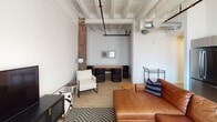 Located at 625 Broadway in downtown San Diego, unit 414 is a single-story loft-style residence that masterfully combines historic industrial character with contemporary design. The living area immediately draws attention with its soaring ceilings accented by exposed white-painted structural beams and striking exposed brick columns that frame large windows, allowing natural light to filter throughout the space. Light wood flooring runs consistently throughout, creating warmth and visual continuity.

The kitchen is efficiently designed with modern flat-front cabinetry in a warm wood-tone finish, light countertops, stainless steel appliances including a range, microwave, and sink, all illuminated by natural light from a window overlooking the building's exterior brick facade.

The bedroom is generously proportioned, highlighted by soaring ceilings with beamed detailing that echo the living area's architectural style. An exposed brick accent wall adds texture and character. The room includes a dedicated walk-in closet, providing practical storage. An adjacent bathroom features a full soaking tub and shower combination with neutral tile surround, wood-look flooring, and brushed nickel fixtures. A separate entry hallway with recessed lighting and a smart thermostat panel completes this thoughtfully designed urban residence.
