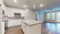 This single-story residence in Myakka City, Florida, presents a clean, contemporary design with a neutral color palette and cohesive finishes throughout. The open-concept kitchen serves as the heart of the home, anchored by a substantial center island topped with speckled granite countertops and illuminated by stylish pendant lights. White shaker-style cabinetry lines the walls, complemented by a geometric gray tile backsplash and under-cabinet lighting. Stainless steel appliances, including a French door refrigerator, electric range, over-the-range microwave, and dishwasher, complete the well-equipped space.

Wood-look luxury vinyl plank flooring extends seamlessly from the kitchen into the open living area, which features recessed lighting, a ceiling fan, and a window allowing natural light to filter in. The entry hallway connects the main living spaces efficiently, with clean white doors and ample closet access.

The primary bathroom includes a granite-topped vanity, a soaking tub with subway tile surround, and direct access to a walk-in closet with built-in wire shelving. A secondary bathroom mirrors the same refined aesthetic with a floating vanity and wood-look flooring. Throughout, the space maintains a bright, move-in-ready atmosphere with consistent modern finishes.