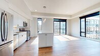 This single-floor residence showcases a clean, contemporary design throughout its well-organized layout. The open-concept kitchen and living area forms the heart of the space, where warm hardwood flooring extends seamlessly underfoot. The kitchen is outfitted with stainless steel appliances, including a gas range, microwave, and French door refrigerator, complemented by white cabinetry, a marble-style backsplash, gold-accented hardware, and a generously sized central island with a white countertop. A pendant light cluster adds a refined focal point above the island.

The living area is bright and open, benefiting from abundant natural light streaming through large, black-framed floor-to-ceiling sliding glass doors that offer views of the surrounding urban landscape. The bedrooms continue the modern aesthetic, with carpeted flooring in at least one room and direct access to outdoor views via expansive windows.

Two bathrooms are finished in a minimalist style, each featuring white vanities with ample storage, white countertops, light tile flooring, and large mirrors. The primary bathroom includes a glass-enclosed tiled shower. A dedicated laundry area houses a full-size GE front-loading washer and dryer with overhead shelving, adding everyday convenience to this thoughtfully designed space.