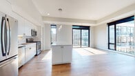 This single-floor residence showcases a clean, contemporary design throughout its well-organized layout. The open-concept kitchen and living area forms the heart of the space, where warm hardwood flooring extends seamlessly underfoot. The kitchen is outfitted with stainless steel appliances, including a gas range, microwave, and French door refrigerator, complemented by white cabinetry, a marble-style backsplash, gold-accented hardware, and a generously sized central island with a white countertop. A pendant light cluster adds a refined focal point above the island.

The living area is bright and open, benefiting from abundant natural light streaming through large, black-framed floor-to-ceiling sliding glass doors that offer views of the surrounding urban landscape. The bedrooms continue the modern aesthetic, with carpeted flooring in at least one room and direct access to outdoor views via expansive windows.

Two bathrooms are finished in a minimalist style, each featuring white vanities with ample storage, white countertops, light tile flooring, and large mirrors. The primary bathroom includes a glass-enclosed tiled shower. A dedicated laundry area houses a full-size GE front-loading washer and dryer with overhead shelving, adding everyday convenience to this thoughtfully designed space.