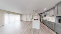 This single-story home showcases a thoughtfully updated interior with a cohesive modern aesthetic carried throughout every room. Light wood-style luxury vinyl flooring flows continuously across the open-concept living and kitchen areas, contributing to a bright, airy feel enhanced by recessed lighting overhead.

The kitchen is a standout feature, equipped with gray shaker-style cabinetry extending to the ceiling for generous storage, white quartz countertops, a subway tile backsplash, stainless steel appliances including a refrigerator and dishwasher, an undermount sink with a contemporary faucet, and a central island with a gas cooktop topped by a stainless steel range hood. The open layout connects the kitchen seamlessly to the living area, which includes a fireplace and a sliding glass door that invites natural light.

The bedrooms are well-proportioned, each featuring ceiling fans with light fixtures, neutral wall tones, and sliding closet doors. One bedroom offers an additional sliding glass door with outdoor access.

Two bathrooms serve the home: one features a tub-shower combination with white tile surround and gray vanity with quartz countertops, while the second includes a walk-in glass-enclosed shower, a wide vanity with dual sinks, quartz countertops, and a well-lit mirror. Both bathrooms maintain the same clean, contemporary finishes found throughout the home.