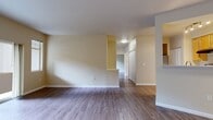 This 770-square-foot, single-floor residence at 14730 Main St in Mill Creek, WA offers 2 bedrooms and 1 bathroom across a thoughtfully designed layout. The living room is a welcoming focal point, featuring a built-in fireplace flanked by an arched niche and sliding glass doors that open to an outdoor patio, filling the space with natural light and views of the surrounding greenery. Wood-style flooring flows consistently throughout the entire unit, lending a clean, cohesive aesthetic. The kitchen is equipped with warm-toned wood cabinetry, stainless steel appliances including a gas range and refrigerator, and a peninsula breakfast bar with pass-through cutouts that connect it visually to the living area. Track lighting illuminates both the kitchen and adjacent dining space. The primary bedroom spans 120 square feet and is served by a dedicated walk-in closet fitted with wire shelving and hanging rods. The second bedroom features a large window with tree-lined views and a built-in baseboard heater. Both bedrooms include panel-style closet doors. The full bathroom offers a tub/shower combination, wood-look tile flooring, and a vanity with warm wood cabinetry. A separate closet provides additional storage within the unit.