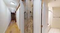 Located on Horseford Road in Lynchburg, Virginia, this single-floor space is a compelling blend of historic architecture and modern renovation. The most striking feature throughout is the exposed original stone masonry walls, which lend an authentic, rustic character to the interior and serve as a dramatic backdrop in both the living and kitchen areas. Complementing the stonework are reclaimed heavy timber beams and posts that span the main living space, adding structural visual interest and a sense of age and craftsmanship seldom found in modern builds.

The open-concept living area features polished concrete floors and ceiling fans, creating an airy, industrial-inspired atmosphere. A kitchen island with a warm wood countertop anchors the kitchen zone, which is outfitted with rich cherry-toned cabinetry, granite countertops, stainless steel appliances including a range, microwave, and refrigerator, and under-cabinet lighting. A hallway off the main living area transitions to a more finished aesthetic, with hardwood flooring and a rustic reclaimed wood plank coat rack mounted between white-paneled walls and doors. The bathroom is clean and functional, featuring white tile flooring, a shower, and crisp white walls. In-unit laundry is also present, adding everyday convenience to this historically rich space.