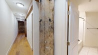 Located on Horseford Road in Lynchburg, Virginia, this single-floor space is a compelling blend of historic architecture and modern renovation. The most striking feature throughout is the exposed original stone masonry walls, which lend an authentic, rustic character to the interior and serve as a dramatic backdrop in both the living and kitchen areas. Complementing the stonework are reclaimed heavy timber beams and posts that span the main living space, adding structural visual interest and a sense of age and craftsmanship seldom found in modern builds.

The open-concept living area features polished concrete floors and ceiling fans, creating an airy, industrial-inspired atmosphere. A kitchen island with a warm wood countertop anchors the kitchen zone, which is outfitted with rich cherry-toned cabinetry, granite countertops, stainless steel appliances including a range, microwave, and refrigerator, and under-cabinet lighting. A hallway off the main living area transitions to a more finished aesthetic, with hardwood flooring and a rustic reclaimed wood plank coat rack mounted between white-paneled walls and doors. The bathroom is clean and functional, featuring white tile flooring, a shower, and crisp white walls. In-unit laundry is also present, adding everyday convenience to this historically rich space.