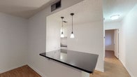 This efficient single-floor, one-bedroom, one-bathroom residence offers a well-designed layout that maximizes every square foot. The living area welcomes you with warm wood-look flooring, neutral white walls, a ceiling fan, and a window fitted with blinds that allows natural light to filter in from outside.

The kitchen is a standout feature, showcasing crisp white cabinetry with sleek bar-pull hardware, striking dark granite countertops, and a peninsula-style breakfast bar that opens toward the living space. Two pendant lights hang above the pass-through, adding a modern touch. The kitchen is equipped with a gas range and an over-the-range microwave, making it both functional and stylish.

The bedroom is a comfortable, well-proportioned room with the same wood-look flooring, a ceiling fan with integrated lighting, and a window with blinds offering outdoor views and natural light.

The bathroom features a full tub and shower combination, a dark-vanity with a white countertop sink, a large mirror, and clean white finishes throughout, creating a tidy and functional space.

Consistent wood-look flooring, ceiling fans, and a cohesive neutral color palette tie all the rooms together, giving the unit a clean, modern aesthetic throughout.