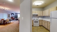 This model unit at Park Station Apartments in Gaithersburg, Maryland presents a thoughtfully arranged single-floor layout accommodating two bedrooms and two full bathrooms within a comfortable footprint. The open living and dining area serves as the heart of the unit, featuring carpet flooring, a bold teal accent wall, and a sliding glass door in the dining space that introduces natural light and outdoor access. The living room benefits from a large window dressed with sheer curtains, creating a bright and inviting atmosphere.

The kitchen is positioned adjacent to the main living area and features light wood cabinetry extending to the upper walls, light-toned countertops, a white coil-burner range with an overhead ventilation hood, and tile flooring that contrasts the carpeted living spaces.

Both bedrooms offer carpeted floors and generously sized windows that allow ample natural light. The primary bedroom includes a walk-in closet fitted with wire shelving and hanging rods. The bathrooms are finished with tile flooring, light wood vanity cabinetry, a large mirror, and a shower-tub combination. Overall, the unit presents a clean, neutral palette with select accent walls adding visual character throughout.