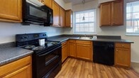 Located at 4037 Lamplighter Dr in Richmond, Virginia, this single-floor residence offers a practical and straightforward layout designed for comfortable everyday living. The kitchen serves as a functional hub of the home, featuring warm honey-toned wood cabinetry, dark countertops, and a full suite of black appliances including an electric range, built-in microwave, and dishwasher. Wood-style flooring runs throughout the kitchen, which also benefits from windows that bring in natural light and views of the surrounding exterior. The kitchen opens toward the main living area, which is finished with plush beige carpeting and includes a wood-floored entryway at the front door. Multiple carpeted bedrooms provide comfortable, quiet spaces, each with windows dressed in blinds that allow for adjustable natural light and white walls that lend a clean, neutral backdrop. At least one bedroom includes a closet with shelving. The bathroom is well-appointed with a full tub-shower combination, wood-style flooring, and a vanity with wood cabinetry. Throughout the home, the consistent use of neutral tones, clean white walls, and warm wood accents creates a cohesive and inviting atmosphere.