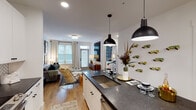 This thoughtfully designed single-floor residence seamlessly blends modern aesthetics with functional living. The open-concept layout connects the kitchen, dining, and living areas into one cohesive space bathed in natural light from large windows and a glass door that opens to the outdoors.

The kitchen is a standout feature, outfitted with crisp white shaker cabinetry, dark granite countertops, a herringbone tile backsplash, and stainless steel appliances including a range, microwave, and refrigerator. A generous center island with an undermount sink and pendant lighting provides both prep space and casual bar seating, making it ideal for entertaining.

The living area offers a relaxed yet stylish atmosphere, with light hardwood flooring, recessed lighting, and ample wall space for art display. A glass-paneled exterior door floods the room with natural light and provides outdoor access.

The bedroom is a comfortable retreat featuring carpet flooring, large windows dressed with bold patterned drapes, and direct access to a spacious walk-in closet with built-in shelving.

The bathroom is clean and functional, featuring dark-topped vanity storage, wood-look flooring, a soaking tub with shower, and convenient access to the adjacent walk-in closet. Throughout the residence, a consistent palette of white walls, black accents, and warm wood tones creates a cohesive and contemporary ambiance.