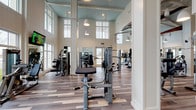 This expansive fitness center is designed to impress both in form and function. The space is defined by its soaring double-height ceilings adorned with a soft blue accent, white shiplap wall paneling, and oversized multi-pane windows that flood the interior with natural light and offer views of the surrounding landscape. Pendant lights hang elegantly throughout, enhancing the bright and airy coastal-inspired aesthetic. Decorative touches, including a mounted kayak and oars, reinforce the resort-style character of the facility.

The fitness floor is finished with multi-tone wood-look flooring and is divided into well-organized zones. The cardio area features a row of Matrix treadmills and ellipticals positioned to face large windows with outdoor views, accompanied by wall-mounted flat-screen televisions. A dedicated cycling studio houses a lineup of Matrix spin bikes with its own TV and direct access to the outdoors via glass double doors. The strength training zone offers a full rack of dumbbells, benches, and a variety of Matrix selectorized machines. A functional training area provides space and equipment for dynamic workouts, including battle ropes and suspension trainers. Full-length mirrors throughout amplify the sense of space and support proper form during exercise.