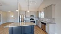 Located at 5347 Niblick Ct in High Point, NC, this single-story home offers a thoughtfully designed layout with modern finishes and quality craftsmanship throughout. The kitchen serves as a central highlight, showcasing soaring vaulted ceilings that create an airy, open atmosphere. Gray shaker-style cabinetry pairs with granite countertops, a tile backsplash, and a full suite of stainless steel appliances, including a refrigerator, range, microwave, and dishwasher. A contrasting navy blue island with its own granite surface provides additional workspace and visual interest, while pendant and track lighting illuminate the space effectively. Hard surface flooring runs throughout the kitchen and common areas, transitioning to plush carpet in the bedrooms. One bedroom features a tray ceiling with crown molding and a ceiling fan, lending an elevated, refined feel, while an additional bedroom offers natural light and a standard ceiling fan. The bathrooms are finished with large-format marble-look tile flooring, dark cabinetry, granite vanity tops, and a tiled tub-surround. A dedicated utility room includes wire shelving, washer/dryer connections, and an electrical panel. The overall design presents a clean, contemporary aesthetic with neutral tones throughout.