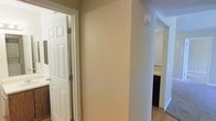 This single-floor space offers a straightforward and functional layout designed for comfortable everyday living. The interior is finished with warm, neutral-toned walls that create a welcoming and cohesive atmosphere throughout. Wood-look flooring runs through the hallway and connecting areas, adding a sense of warmth and continuity to the space.

The hallway serves as the central connector, linking the various rooms with ease. A classic six-panel white door is visible, providing access to an adjoining room — likely a bathroom or utility space — and features a traditional design that complements the understated interior style. The passageway opens toward what appears to be a kitchen area, where darker cabinetry is visible, offering a subtle contrast against the light-colored walls.

Natural and artificial lighting work together to keep the interior bright and open. The clean, minimal aesthetic of the space is consistent throughout, with simple wall finishes and practical fixtures that prioritize function. Overall, this space presents a tidy, move-in ready environment with a no-frills design that provides a solid foundation for personalization and comfortable day-to-day use.