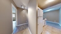 This well-organized single-floor unit in Abbotsford, BC offers a practical and efficient layout across three bedrooms, one bathroom, a kitchen, and a connecting hallway. The interior is finished with a consistent warm taupe colour palette on the walls, complemented by clean white baseboards and textured ceilings throughout.

The hallway serves as the central artery of the unit, featuring tile flooring that transitions into light grey vinyl plank flooring in the main living areas and bedrooms. The kitchen is positioned adjacent to the hallway and includes white appliances — a refrigerator and electric range — alongside tile flooring, offering a functional cooking space.

Each bedroom is finished with the same light grey vinyl plank flooring and features neutral taupe walls, windows fitted with blinds for natural light and privacy, and individual closets with hanging rods for storage. Baseboard heaters are present in the bedrooms, ensuring warmth throughout the colder months.

The bathroom is appointed with full-height beige ceramic tile surrounding the soaker tub and handheld shower, tile flooring, and a vanity with countertop. The space is efficiently designed to maximize utility. Overall, the unit presents a clean, move-in ready interior with consistent finishes throughout.