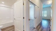 Located at 408 Northampton Rd in Amherst, Massachusetts, this single-floor unit offers a thoughtfully designed layout with modern finishes throughout. The open kitchen is a standout feature, showcasing gray shaker-style cabinetry, granite countertops, a herringbone tile backsplash, and a full suite of stainless steel appliances including a dishwasher, range, microwave, and refrigerator. A built-in desk area adds functional versatility to the kitchen space. Durable hardwood-style flooring runs throughout the unit, complementing the neutral, light-toned walls that create a bright and welcoming atmosphere. Natural light flows in through large windows fitted with blinds, offering views of the surrounding area. The hallway connects the main living spaces with a sliding barn door — a contemporary architectural accent — leading to additional rooms. The bathroom is finished in a clean, all-white palette with a full tub-shower combination, wood-look tile flooring, and chrome fixtures. The bedrooms are well-proportioned, each with windows that invite natural light. The overall design balances modern aesthetics with practical, comfortable living in a move-in ready setting.