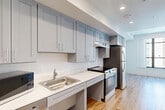 Located at 1370 Harvard St NW in Washington, DC's vibrant Columbia Heights neighborhood, this efficiently designed unit offers a thoughtful layout that maximizes every square foot. Warm hardwood-style flooring runs continuously throughout the space, lending a cohesive and inviting feel.

The kitchen is well-appointed with gray shaker-style cabinetry extending to the ceiling for ample storage, clean white countertops, a classic subway tile backsplash, and a full suite of stainless steel appliances including a refrigerator, electric range, dishwasher, and built-in microwave. The kitchen flows naturally into the living area, which is brightened by a large black-framed window that draws in natural light and offers views of the surrounding neighborhood.

The bathroom is designed with accessibility in mind, featuring sturdy grab bars, a floating vanity with a white countertop, a large mirror, and matching hardwood-style flooring that maintains the unit's consistent aesthetic. The entry corridor provides a clean transition into the living space, complete with recessed and flush-mount lighting throughout. The overall design is modern and neutral, creating a bright, functional, and move-in-ready environment in the heart of Washington, DC.
