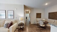This single-story residence is designed with a neutral color palette of warm beige and gray tones throughout, creating a cohesive and calming atmosphere. The open-concept layout connects the living, dining, and kitchen areas seamlessly, promoting an efficient and comfortable flow.

The living room is a well-lit space featuring French doors that allow natural light to fill the room, complemented by a ceiling fan overhead. Dark hardwood-style flooring anchors the area and extends into the dining space, where a round table sits beneath decorative wall art.

The kitchen is outfitted with white shaker-style cabinetry, granite countertops, stainless steel appliances including a range and microwave, and a double basin sink — providing a functional and attractive workspace.

Two bedrooms feature plush carpeting, ceiling fans, and windows with blinds, offering comfortable and private retreats. Each bathroom includes a white vanity with storage, a large mirror, lighted fixtures, and stone-look tile flooring, reflecting a clean and practical design.

A central hallway with closet access connects the private areas of the residence, completing a thoughtfully organized floor plan.