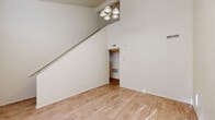 This two-story home offers a thoughtfully organized layout across two floors, combining comfortable living spaces with practical design details throughout. The main floor serves as the heart of the home, featuring a bright and open living room distinguished by dramatic vaulted ceilings and a stylish multi-bulb chandelier. Light wood-style flooring runs through the main living areas, lending warmth and continuity to the space. A staircase rises prominently along one wall, adding architectural character to the open volume. The kitchen is equipped with warm-toned wooden cabinetry, a white electric range, and a full-size refrigerator, with light flooring and a window providing a pleasant, functional cooking environment. The upper floor hosts the bedrooms, each carpeted for added comfort. The primary bedroom is a generously sized retreat featuring a ceiling fan, two windows that invite natural light, and access to a dedicated closet complete with a full-width hanging rod and shelf. A second bedroom includes sliding panel closet doors for convenient storage. Both bathrooms are cleanly finished, with one featuring a full tub-shower combination, wood-tone vanity, and hardwood-style flooring. A dedicated closet provides additional storage, rounding out this well-appointed two-level home.