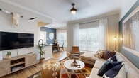 This thoughtfully designed single-floor residence offers three bedrooms, two bathrooms, a dedicated dining room, and a combined kitchen and living area, all connected by a central hallway with closet storage. The open living room is a standout, featuring crown molding, a ceiling fan, large windows with sheer curtains that flood the space with natural light, and a striking teal accent wall anchoring the room. Light hardwood-style flooring flows throughout. The galley-style kitchen is well-appointed with white shaker cabinetry, dark countertops, stainless steel appliances, and a clean, functional layout. Adjacent to the kitchen, the dining area benefits from abundant natural light through oversized windows and features the same bold blue-gray accent wall, creating a cohesive aesthetic. The primary bedroom is a comfortable retreat with a deep teal accent wall, warm lighting, and hardwood flooring. A second bedroom continues the bold design language with a navy accent wall. Both bathrooms feature white vanity cabinetry, dark countertops, and tub-shower combinations. Two closets provide practical storage. The overall ambiance is modern and eclectic, blending rich accent colors with warm neutral tones for an inviting, well-curated feel.