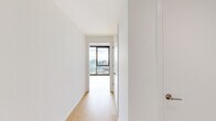 This contemporary high-rise unit offers 2 bedrooms and 1 bathroom across a single floor, thoughtfully designed with clean lines and modern industrial aesthetics. Exposed concrete ceilings contrast beautifully with crisp white walls and light hardwood flooring found throughout, creating a refined urban atmosphere.

The open-plan living area and kitchen are bathed in natural light from expansive floor-to-ceiling windows framed in matte black, offering breathtaking panoramic views of the downtown skyline. The kitchen features light wood cabinetry, stainless steel appliances including a refrigerator, range, and dishwasher, complemented by track lighting mounted on the concrete ceiling.

The spacious primary bedroom is a standout feature, wrapped in floor-to-ceiling glass on two sides, delivering dramatic corner city views. The second bedroom also benefits from large windows with elevated outlooks. A hallway connects the bedrooms to the shared bathroom and closet, while a dedicated entrance provides a welcoming transition into the home.

The unit also includes access to an outdoor balcony showcasing sweeping high-rise views of the surrounding urban landscape. Throughout the space, the interplay of natural light, industrial materials, and city vistas creates a compelling and sophisticated living environment.