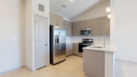 This single-floor residence presents a clean, contemporary design characterized by neutral tones, light wood-look flooring, and an open layout. The kitchen serves as a central highlight, featuring taupe shaker-style cabinetry extending to the ceiling for generous storage, a full suite of stainless steel appliances including a side-by-side refrigerator with ice maker, electric range, and built-in microwave. A peninsula with a white countertop and undermount sink provides additional prep space and acts as a natural divider between the kitchen and living area, complemented by pendant lighting overhead. A subway tile backsplash adds a classic finishing touch.

The bedrooms are bright and well-proportioned, each receiving natural light through windows with neighborhood views. One bedroom features built-in open shelving alongside light wood-look flooring, while another includes plush carpeting, a ceiling fan, and closet access. A spacious walk-in closet with wire shelving and a window offers practical storage.

Two bathrooms serve the unit: one includes a glass-enclosed walk-in shower with large-format tile and gray cabinetry, while the second features a full tub-shower combination, a wide vanity with a white countertop, and a large mirror. Both bathrooms maintain a cohesive, understated palette consistent with the overall aesthetic of the space.