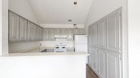 This single-story, 2-bedroom, 1-bathroom home offers a thoughtfully designed layout with a neutral color palette and a mix of practical finishes. The living room serves as the focal point of the home, featuring dramatic vaulted ceilings, a ceiling fan, a tile-surround fireplace, and multiple windows that allow generous natural light to fill the carpeted space. Adjacent to the living area, a dining space with wood-look flooring and a row of large windows provides a bright, open feel, accented by a pendant light fixture.

The kitchen is well-equipped with raised-panel gray cabinetry extending floor to ceiling for ample storage, light countertops, a peninsula with sink, white appliances including a range and refrigerator, and a range hood. The wood-look flooring continues throughout this area, complementing the clean, functional design.

Both bedrooms feature vaulted ceilings with ceiling fans, plush carpeting, and windows that bring in natural light. One bedroom includes two windows and a closet door, while the other offers a more intimate feel with a single window. The overall ambiance of the home is bright, clean, and move-in ready, with consistent finishes creating a cohesive and comfortable living environment.