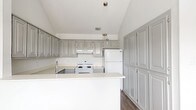 This single-story, 2-bedroom, 1-bathroom home offers a thoughtfully designed layout with a neutral color palette and a mix of practical finishes. The living room serves as the focal point of the home, featuring dramatic vaulted ceilings, a ceiling fan, a tile-surround fireplace, and multiple windows that allow generous natural light to fill the carpeted space. Adjacent to the living area, a dining space with wood-look flooring and a row of large windows provides a bright, open feel, accented by a pendant light fixture.

The kitchen is well-equipped with raised-panel gray cabinetry extending floor to ceiling for ample storage, light countertops, a peninsula with sink, white appliances including a range and refrigerator, and a range hood. The wood-look flooring continues throughout this area, complementing the clean, functional design.

Both bedrooms feature vaulted ceilings with ceiling fans, plush carpeting, and windows that bring in natural light. One bedroom includes two windows and a closet door, while the other offers a more intimate feel with a single window. The overall ambiance of the home is bright, clean, and move-in ready, with consistent finishes creating a cohesive and comfortable living environment.