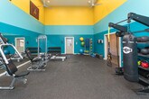 Located at 10 Rimington Lane in Decatur, Georgia, this single-floor fitness facility makes a bold visual statement with its striking teal and gold color scheme across soaring walls and ceilings. The generous open floor plan is finished with durable rubber flooring throughout, providing both safety and comfort during workouts. The space is well-lit by a combination of recessed lighting and overhead fluorescent fixtures, complemented by ceiling fans that keep the environment comfortable during intense training sessions.

The main workout area is comprehensively equipped for a full-body training experience. Cardio options include multiple treadmills and elliptical machines, each with digital displays for performance tracking. Strength training is supported by a cable machine system, a dedicated dumbbell rack spanning a wide range of weights, an adjustable bench, and a variety of functional training tools including kettlebells, medicine balls, stability balls, and TRX suspension trainers. A heavy punching bag and a wall of mirrors further enhance the training versatility of the space.

Atlanta sports team banners — including those for the Atlanta Falcons and Atlanta Braves — adorn the walls, adding a local character to the energetic atmosphere. An adjacent hallway connects to additional rooms, suggesting supporting amenities. The space presents a professional and motivating environment well-suited for serious fitness use.