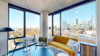 Located at 808 Cleveland in Chicago's vibrant River North neighborhood, this modern multi-bedroom unit offers a thoughtfully designed layout across a single floor. The open living and kitchen area serves as the heart of the space, anchored by dramatic floor-to-ceiling windows that frame sweeping views of the Chicago skyline, including the iconic John Hancock Center. Exposed concrete ceilings and a bold structural column lend an industrial-chic aesthetic, while light wood-tone flooring runs throughout, creating a warm and cohesive feel. The kitchen is outfitted with stainless steel appliances, two-tone cabinetry in light wood and white, subway tile backsplash, and track lighting overhead. All four bedrooms benefit from large windows with impressive elevated city and neighborhood views, filling each room with abundant natural light. The three bathrooms are finished with large-format tile flooring, glass-enclosed walk-in showers with floor-to-ceiling tile surrounds, and dark wood vanities with undermount sinks. A hallway connects the private rooms and includes a stacked in-unit washer and dryer for added convenience. The exposed concrete ceiling detail extends throughout, tying together the space's contemporary industrial character.