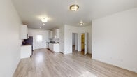 Located at 1800 S Greeley Hwy in Cheyenne, Wyoming, this single-floor unit features a bright, clean aesthetic defined by light wood-style luxury vinyl plank flooring and crisp white walls throughout. The open layout connects a spacious living area to a galley-style kitchen, which is outfitted with white shaker cabinetry, dark marbled countertops, stainless steel appliances including a refrigerator, range, microwave, and dishwasher, and a single-basin sink. A rear door in the kitchen provides direct exterior access and allows natural light to filter in.

The living area is generously proportioned, offering ample room for multiple furniture arrangements, and receives natural light through a large front-facing window. The bedrooms continue the same clean, neutral palette, each featuring light flooring, white walls, and windows with blinds that bring in outdoor views. One bedroom includes a built-in closet with a rod and shelf system. A wall-mounted HVAC unit is present in select rooms, providing individualized climate control.

The bathroom is equipped with a vanity featuring dark marbled countertops, white cabinetry, a toilet, and a full soaking tub with shower. A water heater is housed within the bathroom utility area. Flush-mount light fixtures with warm-toned hardware are used consistently throughout the unit, reinforcing a cohesive and functional design.