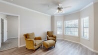 This single-story unit offers a thoughtfully organized layout across a compact yet efficiently utilized floor plan. The living room serves as the centerpiece of the space, featuring crown molding, light wood-style flooring, a ceiling fan with integrated lighting, and multiple windows fitted with slatted blinds that allow natural light to filter in. The neutral, warm-toned walls contribute to an airy and cohesive ambiance throughout.

The kitchen is galley-style and equipped with stainless steel appliances, including a range, microwave, and refrigerator, complemented by warm wood cabinetry and a tile backsplash. Adjacent to the kitchen, a dedicated dining area provides space for casual meals.

The bedroom features carpet flooring, a ceiling fan, and a window with natural light. A walk-in closet with wire shelving offers practical storage. The full bathroom includes a tiled soaking tub and shower combination, wood-tone cabinetry, a vanity, and wood-style flooring. A dedicated laundry area houses a top-loading washer with additional wire shelving above, adding everyday convenience to the unit.