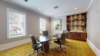 Located at 906 Oasis Palm Circle in Ocoee, Florida, this single-floor amenity facility is thoughtfully designed to support both professional and collaborative needs. The space is defined by a refined aesthetic that blends warm natural materials with contemporary finishes throughout.

The main corridor serves as an inviting thoroughfare, featuring rich hardwood-style plank flooring and a distinctive stained wood plank ceiling with recessed lighting. Crisp white panel doors line the hallway, leading to the individual functional spaces within.

The conference room is an elegantly appointed meeting space outfitted with a sleek dark conference table surrounded by leather executive chairs. A boldly patterned golden botanical carpet anchors the room, while multiple white-shuttered windows allow ample natural light and views to the outside. A stacked stone accent wall with built-in wood shelving adds warmth and visual interest to one corner, complemented by crown molding along the ceiling perimeter.

Adjacent to the conference room, the business center continues the cohesive design language with the same vibrant patterned carpet. Granite-topped workstations line the walls, equipped with desktop computers and teal task chairs. A dramatic textured stone accent wall featuring a decorative peacock art piece serves as a bold focal point, while pendant lighting adds a sophisticated ambiance. Together, these spaces offer a highly functional and visually engaging environment.