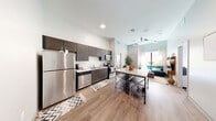 Located at 505 E St Louis St in Springfield, MO, this thoughtfully designed 4-bedroom, 4-bathroom unit offers a contemporary living experience across a single floor. The open-concept kitchen and living area serves as the heart of the space, featuring dark espresso cabinetry, a full suite of stainless steel appliances including a refrigerator, dishwasher, microwave, and range, all set atop light hardwood-style flooring. A marble-top island with bar seating adds both function and style to the kitchen. The living area flows naturally from the kitchen, benefiting from tall ceilings and large windows that invite natural light and offer views of the surrounding streetscape. Each of the four bedrooms is compact yet well-appointed, featuring built-in shelving, individual windows, and plush carpeting. The rooms are designed to maximize efficiency with integrated storage solutions above the bed areas. Every bedroom is paired with its own private en-suite bathroom, each equipped with a walk-in shower, wood-toned vanity, and clean white tile finishes. Additional spaces include a dedicated laundry room and utility room, contributing to the overall functionality of the unit. The consistent modern aesthetic throughout creates a cohesive and comfortable living environment.