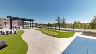 Located in Langford, British Columbia, this rooftop amenity terrace at 1110–1112 McCallum Road offers a thoughtfully designed outdoor retreat with a diverse range of recreational and social features. The terrace is finished with large-format concrete pavers that provide a clean, modern aesthetic throughout the space.

A standout feature is the multi-hole putting green, surfaced with lush artificial turf and framed by curved turf borders that add a sense of organic flow to the layout. Adjacent to the green is a life-sized chess board, complete with oversized black and white pieces, offering an engaging activity for residents and guests alike.

Two pergola-style shade structures anchor the terrace, each outfitted with seating areas suited for both casual lounging and outdoor dining. The structures feature sleek dark steel framing that complements the contemporary architectural character of the building. Planter boxes with ornamental grasses add greenery and definition throughout the space.

The terrace is enclosed by a glass-panel railing system, preserving unobstructed panoramic views of the surrounding tree canopy, rolling hillsides, and neighbouring Langford skyline. The open-air design ensures abundant natural light throughout the day, creating a bright and inviting atmosphere. This rooftop terrace delivers a well-rounded amenity experience combining leisure, recreation, and scenic outdoor living.