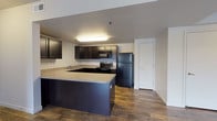 This single-floor residence offers a thoughtfully designed layout that balances open communal spaces with comfortable private quarters. The kitchen is a standout feature, showcasing dark espresso-toned cabinetry paired with light granite-style countertops and a full suite of black appliances, including a refrigerator, electric range, built-in microwave, and a double-basin stainless steel sink. A peninsula counter extends the workspace and creates a natural transition into the living area. The open living and dining space is bright and welcoming, featuring rich wood-look plank flooring, a ceiling fan with light fixture, and sliding glass doors that invite natural light and provide access to an outdoor area. The bedrooms offer a contrast in texture, with plush carpeting underfoot and windows fitted with blinds for privacy and light control. The bathroom is clean and functional, featuring dark cabinetry with a granite-style vanity top, a large mirror, and a full shower-tub combo. Throughout the residence, neutral wall tones, white trim, and consistent flooring choices create a cohesive and modern aesthetic that is both practical and inviting.
