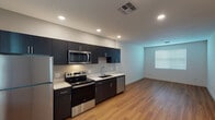 This single-floor space showcases a clean, contemporary design with a thoughtful layout and quality finishes throughout. The open-concept kitchen and living area serves as the heart of the unit, featuring rich dark cabinetry, crisp white countertops, and a full suite of stainless steel appliances including a refrigerator, electric range, over-the-range microwave, and dishwasher. Warm-toned hardwood flooring extends across the kitchen and living area, lending a welcoming and cohesive feel to the space.

The bedrooms offer a comfortable contrast with plush wall-to-wall carpeting and neutral walls that create a calm, restful atmosphere. Natural light filters in through windows fitted with horizontal blinds. At least one bedroom includes a built-in closet with a shelving system, providing practical storage solutions.

The bathroom is well-appointed with a tub and shower combination, a sleek dark-toned vanity with a white countertop, an oval mirror, and a bright vanity light fixture above — all set against light-colored walls and hardwood-style flooring. Recessed lighting throughout the unit ensures even, modern illumination. Overall, the space presents a fresh, move-in-ready environment defined by its modern aesthetic and functional design.